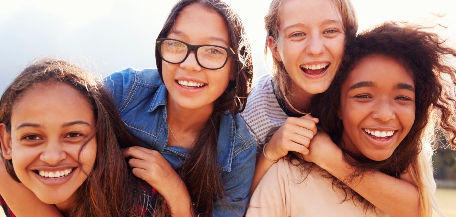 Four teenage girls having fun piggybacking outdoors