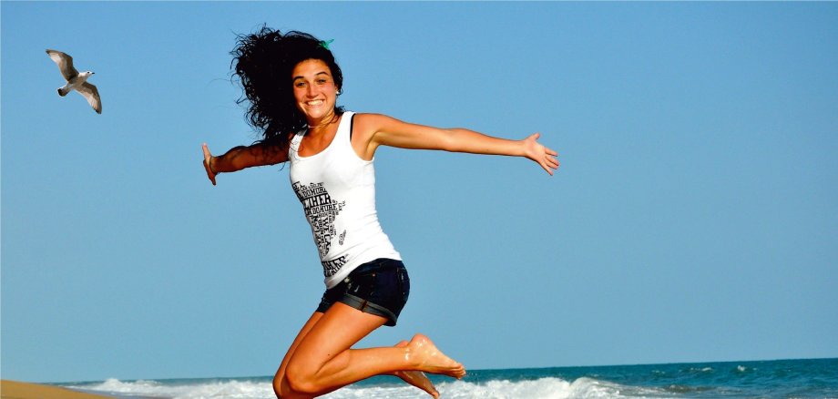 Junges Mädchen in Shorts und weißem T-shirt mit langen braunen Strand springt hoch am Strand.
