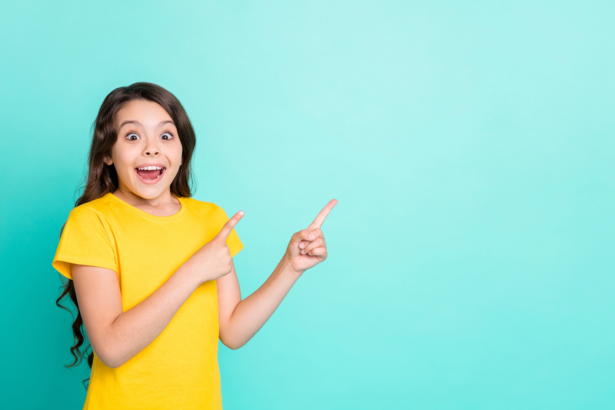 Fröhliches Mädchen in gelbem T-Shirt zeigt nach rechts.